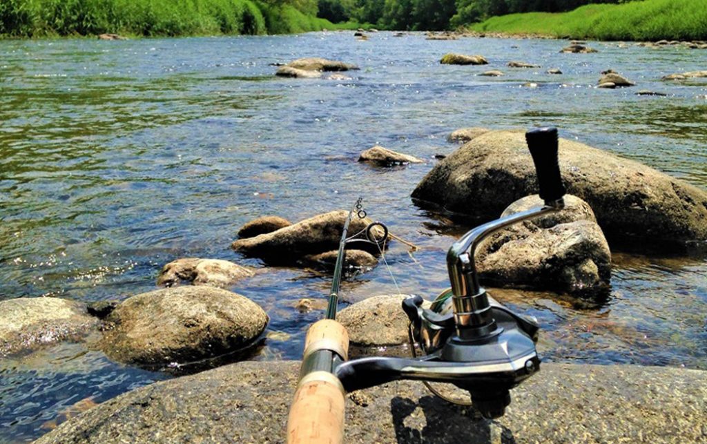 川辺にて岩に沖竿をしてロッドの付け根から先端に向かって撮影